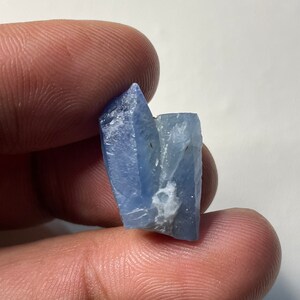 May include: A cluster of blue, translucent crystals with a rough, natural texture. The crystals are pointed and have a slightly cloudy appearance.