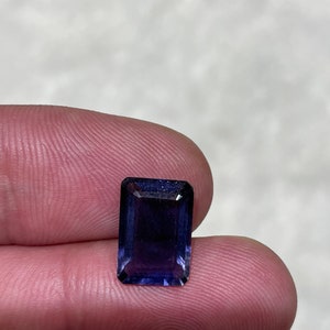 Puede incluir: Una piedra preciosa de color morado oscuro, con un corte rectangular y un acabado facetado.