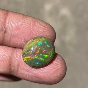 Puede incluir: Una piedra preciosa de ópalo verde, marrón e iridiscente con forma ovalada redondeada.