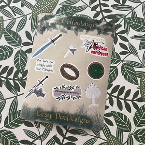 May include: A sheet of stickers featuring characters and objects from the Lord of the Rings. The stickers are on a white background with green leaves. The text on the stickers includes "Fellowship", "I can't carry it for", "Not can carry you!" and "I'm going on an adventure!"
