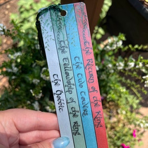 May include: A bookmark with a green, blue, and red striped background. The bookmark has the text "The Return of the King", "The Two Towers", "The Fellowship of the Ring", and "The Hobbit" written in black ink.