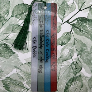May include: A bookmark with a green tassel, featuring the titles of the Lord of the Rings books: "The Return of the King", "The Two Towers", "The Fellowship of the Ring", and "The Hobbit".