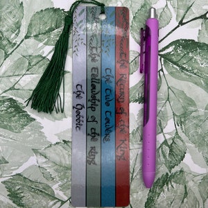 May include: A bookmark with a green tassel, featuring the titles of the Lord of the Rings books: "The Return of the King", "The Two Towers", "The Fellowship of the Ring", and "The Hobbit".