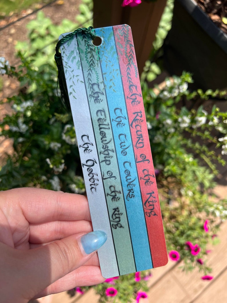 May include: A bookmark with a green, blue, and red striped background. The bookmark has the text "The Return of the King", "The Two Towers", "The Fellowship of the Ring", and "The Hobbit" written in black ink.