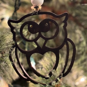 May include: A black wooden owl ornament with a heart cutout, hanging from a white bead and twine on a Christmas tree.