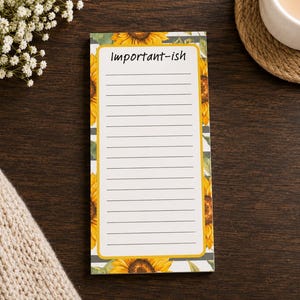 May include: A rectangular notepad featuring a sunflower pattern border with green leaves on a gray striped background. The center is a white area with horizontal lines and the text Important-ish printed in black at the top of the page.