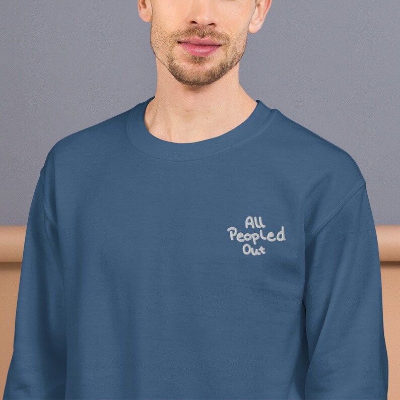 Pode incluir: Uma camisa de frio azul escura com o texto "All People Out" bordado em branco na frente.