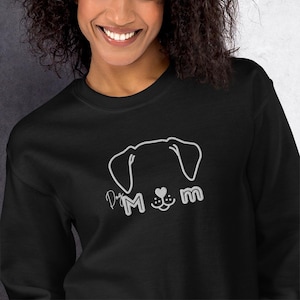 May include: Black sweatshirt featuring a white outline of a dog's face with the text "Dog Mom" in a script font. The design includes a heart and paw print. The sweatshirt is made of a soft material.