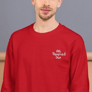 Pode incluir: Camisola de cor vermelha com o texto "All People Out" bordado a branco na frente.