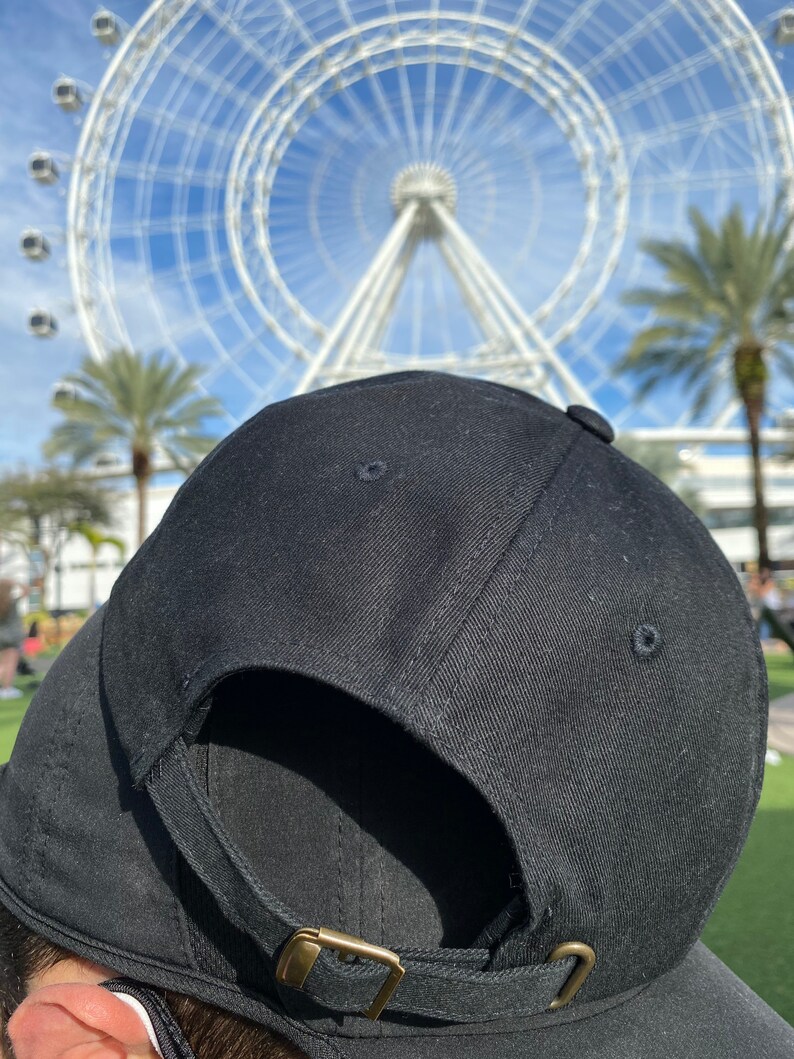 May include: A black baseball cap with a brown adjustable strap and buckle. The cap is made of a soft, textured fabric.