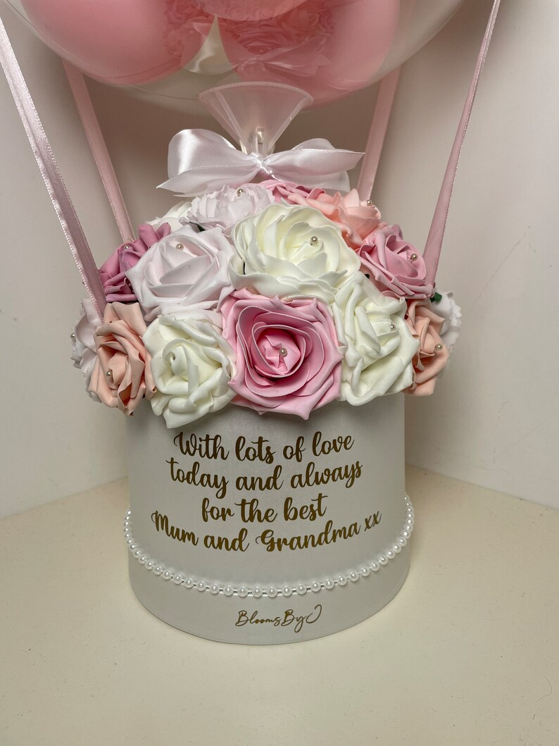 Puede incluir: Arreglo floral en una caja redonda blanca, con rosas rosas, blancas y melocot&oacute;n. La caja est&aacute; adornada con perlas y tiene el mensaje: "With lots of love today and always for the best Mum and Grandma xx". Un globo rosa est&aacute; suspendido arriba.