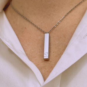 Könnte beinhalten: Eine silberne Halskette mit einem langen, rechteckigen Anhänger. Der Anhänger hat ein kleines Herz eingraviert.