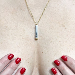 May include: A gold chain necklace with a rectangular pendant. The pendant is silver with a gold-coloured bottom. The necklace is displayed on a person's chest.