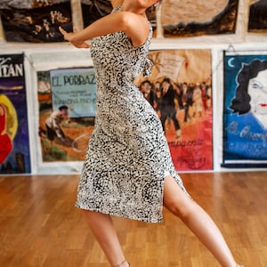 May include: A woman wearing a black and white animal print dress with a side slit. She is wearing nude heels and is posing with her arms outstretched.