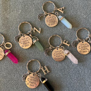 May include: Five silver keychains with a charm that says "I love you to the moon and back" and a crystal charm. Each keychain has a different letter charm: A, Z, F, H, and N.