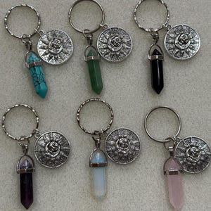 May include: Six silver keyrings with a silver charm featuring a sun and moon design and a crystal pendant. The crystals are turquoise, green, black, purple, white, and pink.