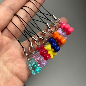 May include: A selection of colourful gummy bear charms in shades like blue, pink, and yellow. Each charm is connected to a black cord with a silver-tone metal clasp. The charms are small and translucent.