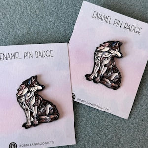 May include: Two enamel pin badges featuring a stylised wolf design with intricate geometric patterns in shades of brown, grey, and white. Each pin is attached to a white display card printed with the text ENAMEL PIN BADGE and BOBBLEANDBOOGIFTS.