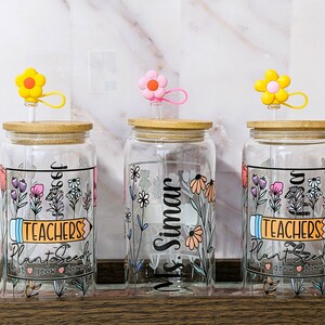 May include: Three glass jars with bamboo lids and colorful flower straws. Each jar has a different design with floral patterns and text. The text on the jars reads "Teachers Plant Seeds That Grow Forever", "Ms. Simar", and "Teachers Plant Seeds That Grow Forever".