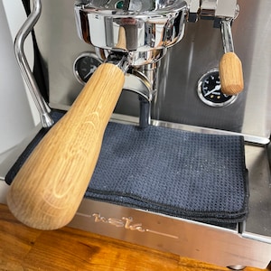 Puede incluir: Primer plano de una máquina de espresso plateada con un mango de madera y una alfombra negra. La máquina tiene un manómetro y una palanca. La máquina está etiquetada como "meta".