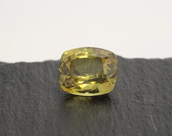 Peut inclure: Une pierre précieuse jaune de taille coussin avec une surface facetée. La pierre précieuse est posée sur un fond gris foncé.