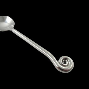 May include: A silver serving spoon with a spiral handle. The spoon has a rounded bowl and a long, curved handle that ends in a decorative swirl. The spoon is made of a shiny, reflective metal.