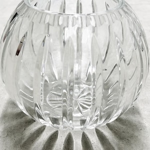 May include: A clear, spherical glass bowl featuring vertical, elongated cut-glass facets that create a repeating pattern around the exterior. The base of the bowl displays a starburst design, and the rim is smooth and circular.