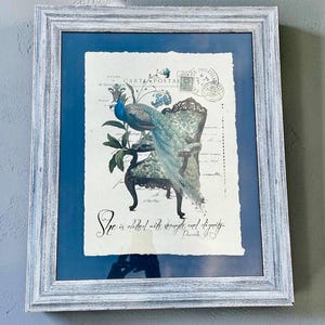 May include: A framed wall art piece featuring a peacock perched on an ornate chair against a vintage postcard background. The print includes the text "She is clothed with strength and dignity" and "Proverbs 31:25" in black script within a distressed white frame.