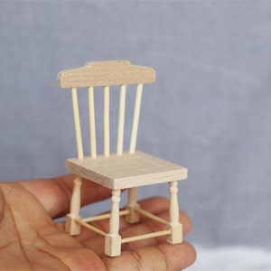 May include: A miniature wooden chair with a slatted back and turned legs. The chair is unfinished and has a natural wood color.