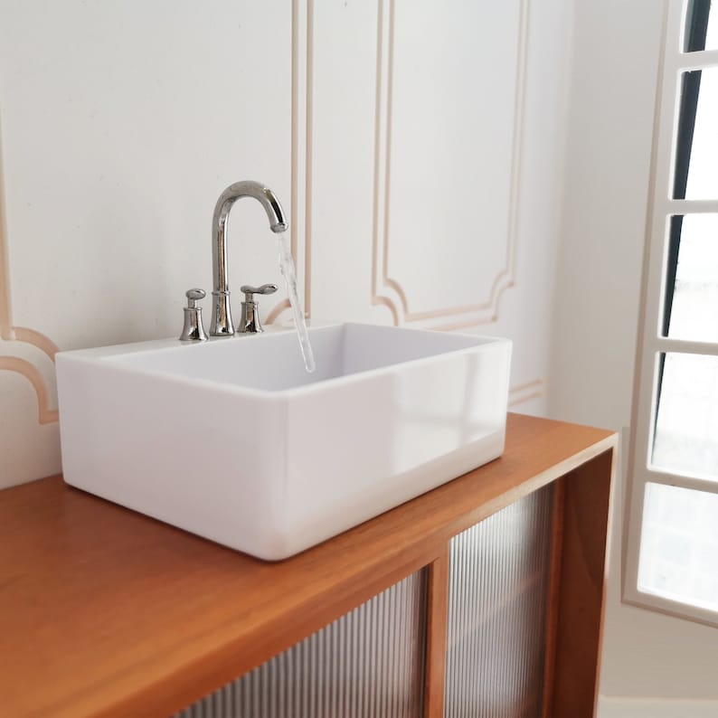 May include: A white porcelain bathroom sink with a chrome faucet and a stream of water flowing from the spout. The sink is mounted on a wooden countertop with a cabinet below.