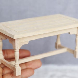 May include: A miniature wooden table with a simple design. The table has a rectangular top and four legs with turned details. The table is made of unfinished wood and is ready to be painted or stained.