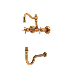 May include: Antique brass kitchen tap set with a curved spout and cross-handle controls. The set includes a wall-mounted tap and a separate curved pipe. The fixtures have a vintage, aged appearance.