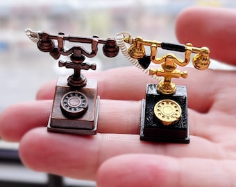 May include: Two miniature rotary dial telephones, one with a black base and gold accents, and the other with a brown base and silver accents. Both phones have a white cord.