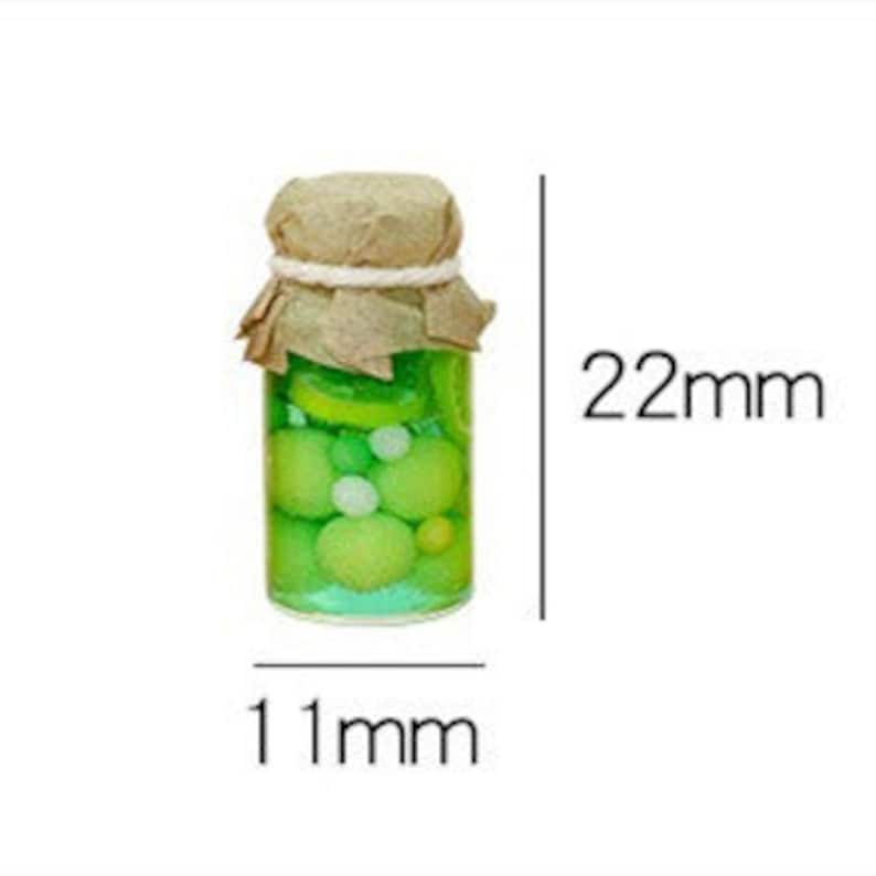 Pu&ograve; includere: Un barattolo di vetro in miniatura con un coperchio di carta marrone e spago, riempito di liquido verde e sfere gialle e bianche. Il barattolo &egrave; largo 11 mm e alto 22 mm.