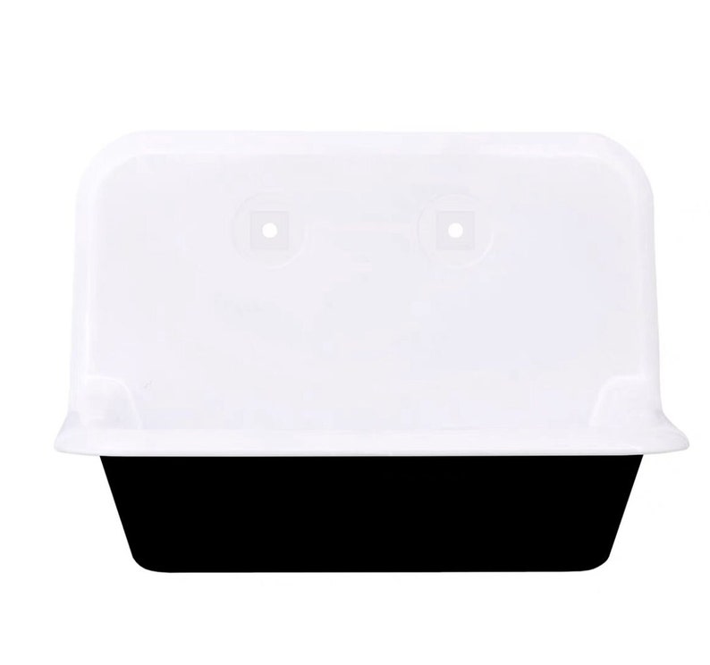 May include: A white plastic container with a black base. The container has a rectangular shape with rounded corners and a slightly curved lid. Two small square holes are visible on the lid.