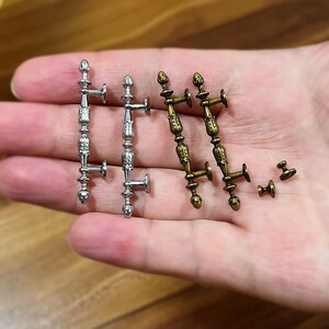 以下が含まれることがあります： ミニチュアの銀とブロンズのキャビネット金具。銀色のハンドルは、詳細で装飾的なデザインです。ブロンズのハンドルは、ヴィンテージ仕上げの同様のデザインです。完全なセット用の小さなノブが含まれています。ドールハウスやクラフトプロジェクトに最適です。