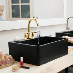 May include: A black porcelain sink with a gold faucet and two handles. The faucet is turned on and water is flowing into the sink.
