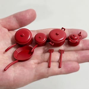 May include: A set of miniature red kitchen cookware, including pots, pans, and spatulas. The set is made of plastic and is designed for pretend play.