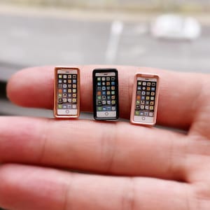 以下が含まれることがあります： 3つの異なる色のミニチュア携帯電話モデル：ゴールド、ブラック、ローズゴールド。各電話には、カラフルなアイコンのグリッドが表示された画面があります。