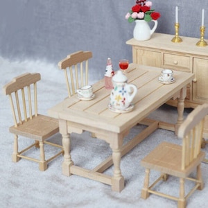 May include: A miniature wooden dining set with a table and four chairs. The table has a light wood finish and is set with a teapot, two cups, and a bottle of wine. The chairs are also made of light wood and have a simple design.