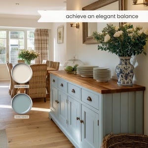 May include: A light blue sideboard with a wooden countertop, drawers, and cabinet doors. A vase with white and blue floral patterns holds white flowers. The text "achieve an elegant balance" is visible. The room has a wooden floor and a dining table.