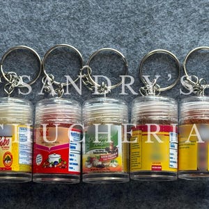 May include: Five spice keychains with clear plastic containers filled with various spices. Each keychain has a silver ring and a label with text and nutritional information. The labels are in various colors, including yellow, red, and green.