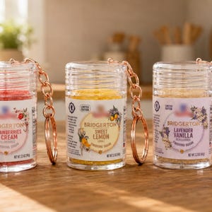 Pode incluir: Três recipientes cilíndricos transparentes cheios de açúcar colorido, cada um com um porta-chaves em ouro rosa. Os rótulos dizem Bridgerton Strawberries & Cream, Sweet Lemon e Lavender Vanilla, com um peso líquido de 94 gramas por unidade.