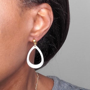 May include: A pair of white teardrop-shaped earrings with a gold accent at the top. The earrings are dangling from the earlobe.
