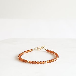 May include: A delicate gold bracelet with small, faceted carnelian beads. The bracelet is made with a simple clasp.