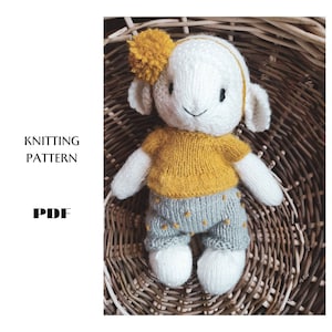 May include: Knitting pattern PDF for a white knitted lamb toy wearing a yellow shirt and grey trousers with yellow dots. The lamb is sitting in a wicker basket.