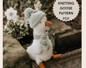 May include: Knitted goose toy wearing a blue and white hat with a pom pom and a green scarf. The goose is sitting on a rock with a green plant in the background. The image includes the text "Knitting Goose Pattern PDF".