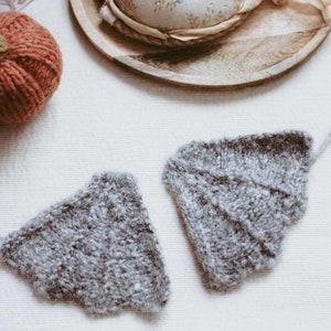 May include: Two gray knitted wings with a scalloped edge, lying on a white fabric surface. The wings are made of a soft, fluffy yarn.