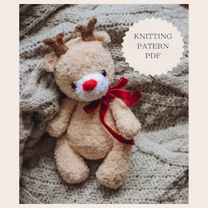 May include: Knitting pattern PDF for a beige crocheted reindeer toy with red antlers and a red bow. The reindeer has a white face with a red nose.