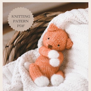 Pode incluir: Padrão de tricô PDF para um brinquedo de gato de crochê laranja e branco. O gato está deitado em um cobertor branco em uma cesta de vime.